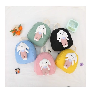 Flat lay showing five colorful kids canvas backpacks with 3D plush bunny decorations