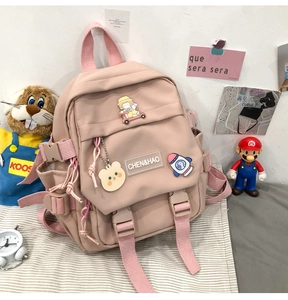 Détail du sac à dos en nylon rose avec un porte-clés ours et des écussons colorés