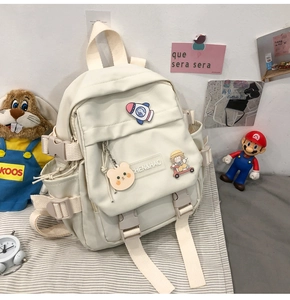 Vue détaillée du sac à dos scolaire blanc crème avec épinglettes, ourson et boucles