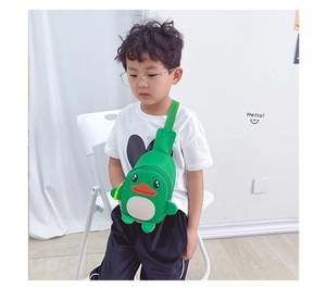 Detail view of a green cartoon duck chest bag worn by a child in a minimalist indoor setting