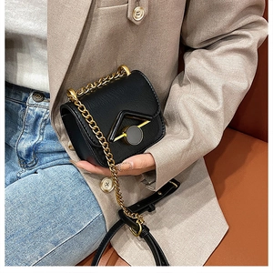 Dettaglio di una mini borsa a tracolla in pelle nera con fibbia dorata a V e catenella