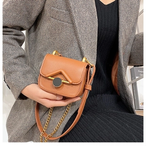 Dettaglio mini borsa a tracolla marrone con chiusura a V dorata e catena su libri di moda