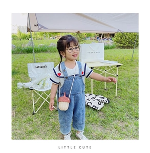 Detail of baby girl outfit with denim overalls, white heart tee and woven acorn crossbody bag