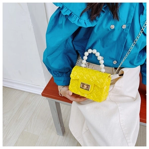 Detail view of yellow jelly mini bag with pearl handle and woven texture on model