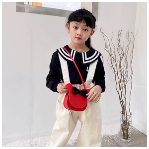 Detail shot of a bright red felt kids' crossbody bag featuring a cute black bow design