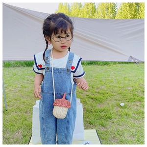 Detail of a cute woven acorn-shaped crossbody bag on a child's denim overall outfit