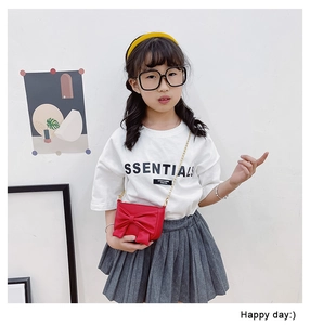 Detail of child wearing red bow crossbody bag with gold metal chain on white background
