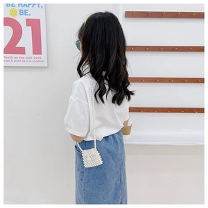 Detail of a girl wearing a white beaded pearl crossbody bag with a chain strap