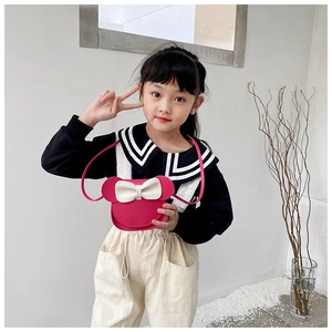 Detail view of a pink bow mini crossbody bag worn by a child in a minimalist setting
