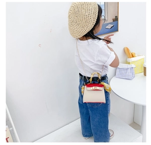 Dettaglio di bambina con borsa crema e rossa con foulard arancione e catena dorata