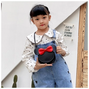 Front view of a black bow-tie crossbody bag worn by a young girl in a bright setting