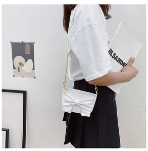 Close-up of girls white crossbody bag with large bow and gold heart charm chain