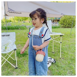 Detail of cute acorn-shaped woven crossbody bag on a child outfit in outdoor setting