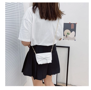 Girl wearing white crossbody bag with large bow and gold chain on black skirt
