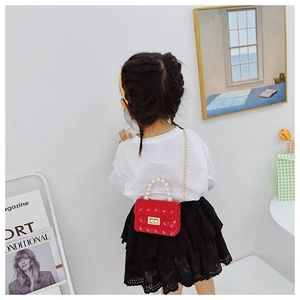 Close-up of red jelly crossbody bag for girls with pearl handle and metal chain strap