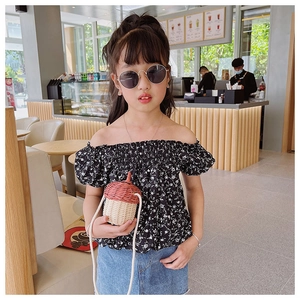 Detail of child wearing a black floral off-shoulder top with an acorn straw bag