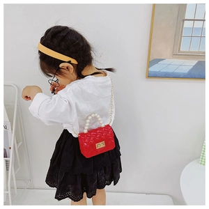 Detail of red quilted jelly mini bag with pearl handle and golden chain for girls