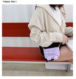 Detail of purple mini crossbody bag with oversized bow and golden metal chain strap