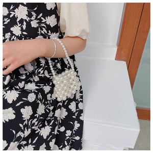 Detailed view of handmade mini pearl beaded handbag with elegant floral dress backdrop