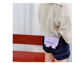 Detail of light purple girls' crossbody bag featuring a large bow and gold chain strap