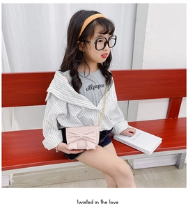Close-up of pink girls bow crossbody bag with gold chain strap worn by a young child