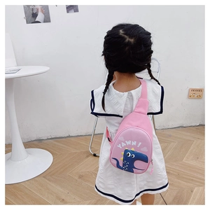 Pink child dinosaur crossbody bag with cartoon print shown on girl in home setting