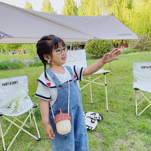 Pink acorn-shaped woven crossbody bag for kids displayed in a scenic outdoor camping setting