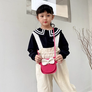 Cute girls pink crossbody bag with white bow knot shown on child model in soft light