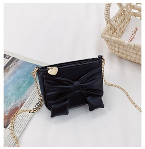 Detail of black faux leather mini crossbody bag featuring a large bow and gold heart charm