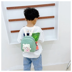 Close-up of mint green mini backpack with cute plush bear charm on an Asian boy