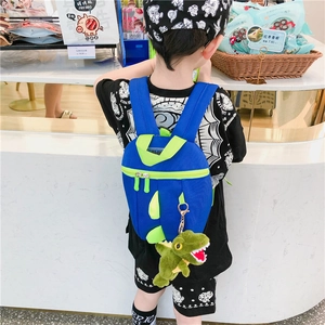 Sac à dos dinosaure bleu avec piques néon et peluche porté par un enfant au dos