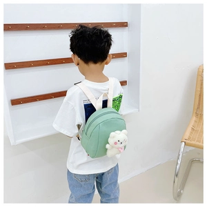 Toddler in a white shirt wearing a light green canvas backpack with a 3D plush teddy bear