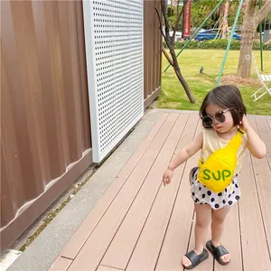 Outdoor shot of a bright yellow kid's canvas crossbody bag featuring green SUP lettering