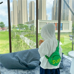 Kid's green canvas crossbody chest bag with yellow SUP letters worn in outdoor setting