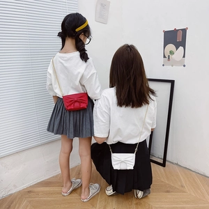 Kids bow crossbody bag with gold chain strap shown in red and white on models