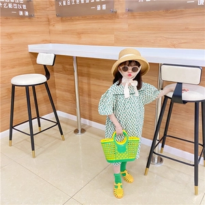 Detail of yellow hollowed-out beach basket bag paired with green geometric kid dress