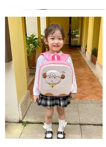 Pink cartoon sheep backpack for kids shown with a child model in a scenic outdoor setting