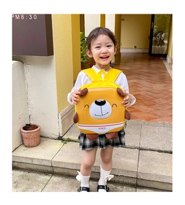 Outdoor shot of a toddler carrying a yellow bear-shaped hardshell cartoon backpack