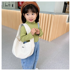 Kid modeling a white canvas shoulder bag with black Hey print in a modern store setting