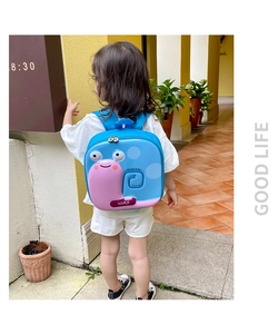 Outdoor shot of a toddler wearing a light blue snail shell backpack with pink accents