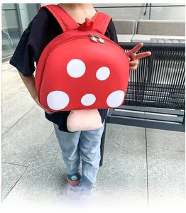Toddler mushroom backpack with red hard shell and white polka dots on model in park