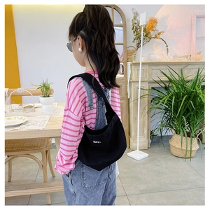 Detailed view of kids' black canvas crescent bag with white letter print on a young model