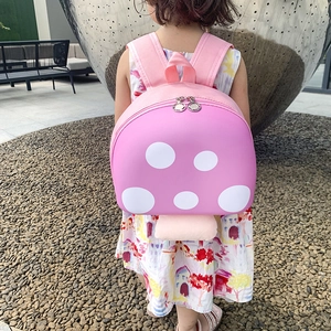 Pink mushroom-shaped preschool backpack for kids with white polka dots on outdoor model