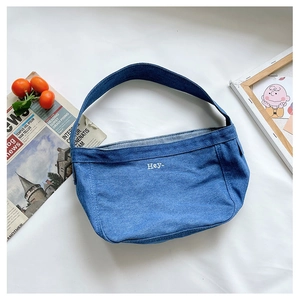 Detailed top view of a blue denim shoulder bag with white Hey embroidery and styling props