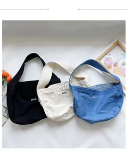 Close-up of small canvas handbags in black, off-white, and denim blue with Hey embroidery