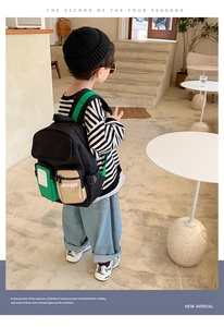 Rear view of a child wearing a black and green color-block backpack in a modern studio