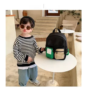Kids black backpack with green and beige pockets modeled in a cafe setting
