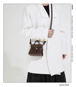 Detail of a dark brown mini crossbody bag with a slim strap and gold logo lettering