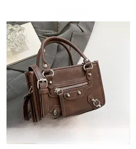 Close-up of vintage brown leather handbag featuring metallic rivets and detailed zippers