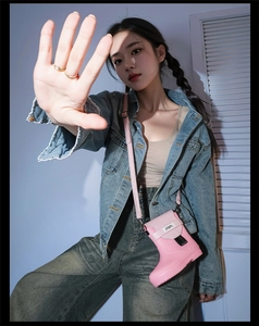 Detailed view of creative pink boot-shaped crossbody bag with logo on a denim jacket